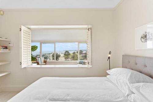 a white bedroom with a bed and a window at Clovelly Beach House - Sea, Sand and Exclusivity in Sydney