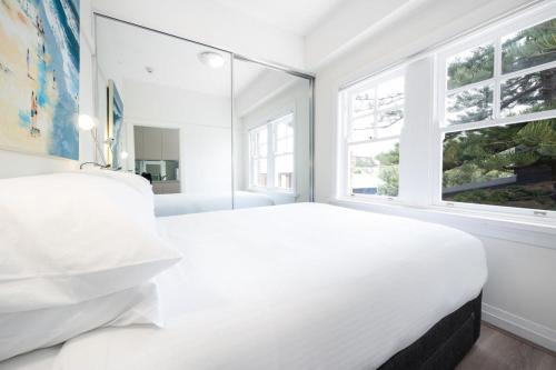 a white bedroom with a large bed and windows at Snug 1-Bed Unit Across from Bondi Beach in Sydney