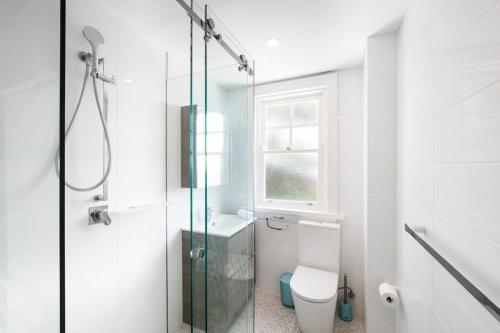a white bathroom with a shower and a toilet at Snug 1-Bed Unit Across from Bondi Beach in Sydney