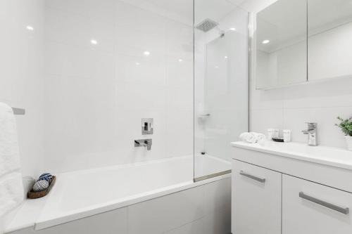 a white bathroom with a shower and a sink at Chic 2-Bed Unit Fully Renovated in Prime Location in Sydney