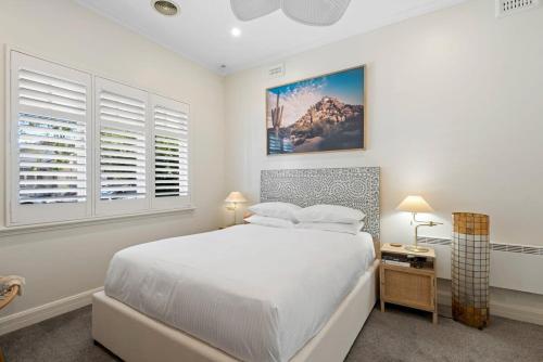 a white bedroom with a large bed and two windows at Sophisticated 2-Bed House with a Pool in Seddon