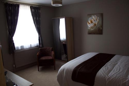 a bedroom with a bed and a chair and a window at The Clyffe Hotel in Lowestoft