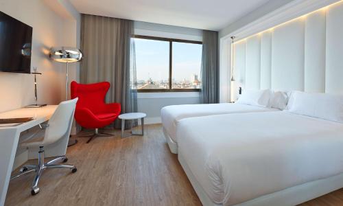 バルセロナにあるNH Collection Barcelona Gran Hotel Calderonの白いベッド、デスク、赤い椅子が備わる客室です。