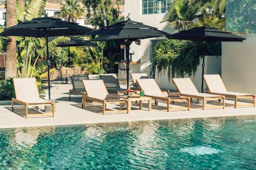 eine Gruppe von Stühlen und Sonnenschirmen neben einem Pool in der Unterkunft Hotel Estefania Boutique Suites in Los Cristianos