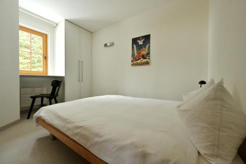 a white bedroom with a large white bed and a chair at Chesa Igna in Arosa