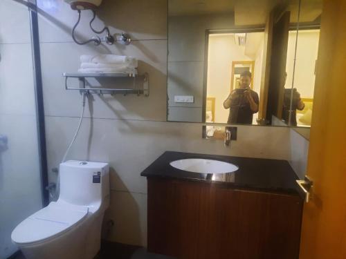 a person taking a picture of a bathroom with a toilet and a mirror at CORPORATE STAY SOLUATION GANDHINAGAR B/53 in Gandhinagar