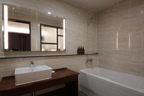 a bathroom with a sink and a tub and a mirror at Hotel J's in Gumi