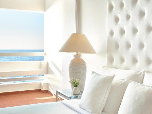 um quarto com uma cama e um candeeiro sobre uma mesa em Grecotel LUX.ME White Palace​ em Adelianos Kampos