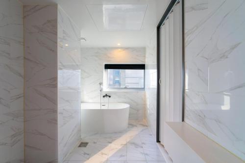 ein weißes Bad mit einer weißen Badewanne und einem Fenster in der Unterkunft Gray 193 Hotel in Busan