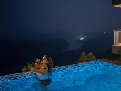 a woman sitting in a swimming pool at night at Ragamaya Resort & Spa Munnar in Munnar