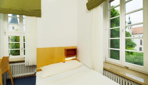 a bed in a room with two windows at Bildungshaus Neckarelz in Mosbach