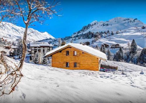 uma cabana de madeira na neve com montanhas ao fundo em Chalet Sicoria - Les Congères em Le Grand-Bornand