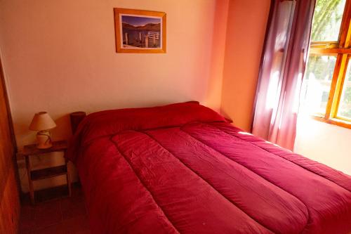 a red bed in a room with a window at Costa del Río in Lago Puelo