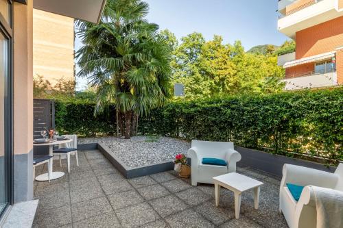 un patio con sillas, mesas y una palmera en Lake Modern Suites - Free Parking, en Lugano