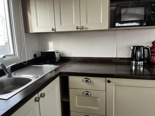 a kitchen with a sink and a microwave at Ger-Y-Bwlch - Spacious static on 5star site with Swimming Pool in Benllech