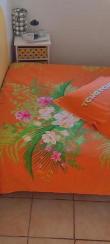 a bed with an orange bedspread with flowers on it at flech kann in Fort-de-France