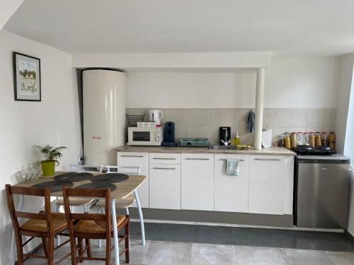 une cuisine avec des armoires blanches et une table avec des chaises dans l'établissement Maison de ville, à La Cressonnière