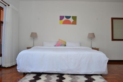 Kutenga Guest House في مابوتو: غرفة نوم مع سرير أبيض كبير مع سجادة