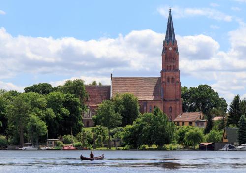 a man in a boat on the water in front of a church at Landhaus Müritzgarten Hotel garni in Röbel