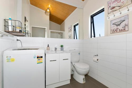 a white bathroom with a toilet and a sink at Sunnyside Spa Retreat - Mangawhai Holiday Home in Mangawhai