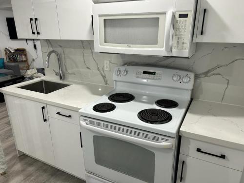 cocina blanca con fogones y microondas en Large Separate Entrance Basement Unit 2Beds 1Washroom Sleeps 4-6, en Pickering