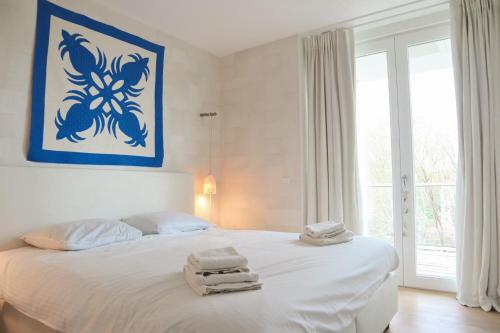 Un dormitorio con una cama blanca con toallas. en Badhuis Dunes, Boulevard de Wielingen 2 en Cadzand