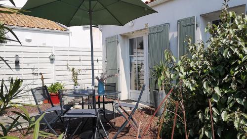un patio avec une table et un parasol vert dans l'établissement Maison PASSIFLORE, à Saint-Denis-dʼOléron