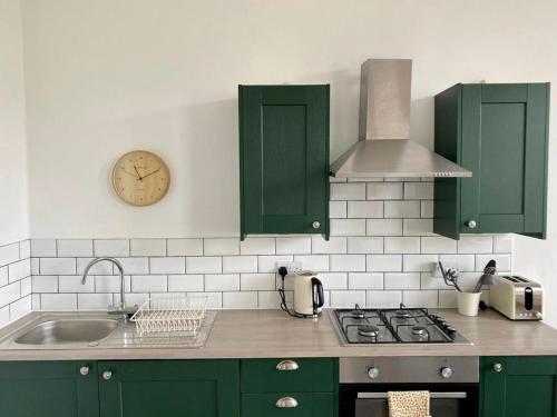 uma cozinha com armários verdes e um relógio na parede em Apartment 3 St Georges em Cheltenham