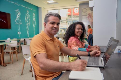 a man and a woman sitting at a table with a laptop at Mega Moda Goiania Hotel in Goiânia