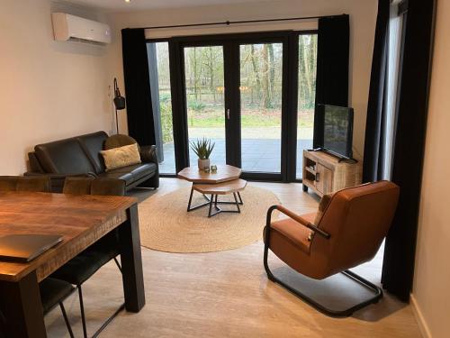 un soggiorno con un divano, un tavolo e una televisione di Schitterend 6 persoons chalet met HOTTUB aan de bossen van Putten a Putten