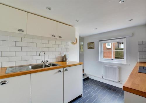a kitchen with white cabinets and a sink and a window at BackToFront Cottage in Briston