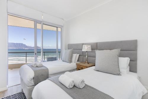 two beds in a bedroom with a view of the ocean at Portico 704 in Bloubergstrand