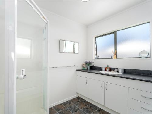 a white bathroom with a sink and a mirror at Beach Life - Whangamata Holiday Home in Whangamata