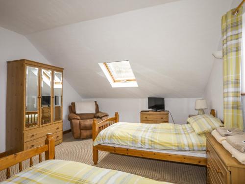 a bedroom with two beds and a chair at Beech Tree Cottage in Caernarfon