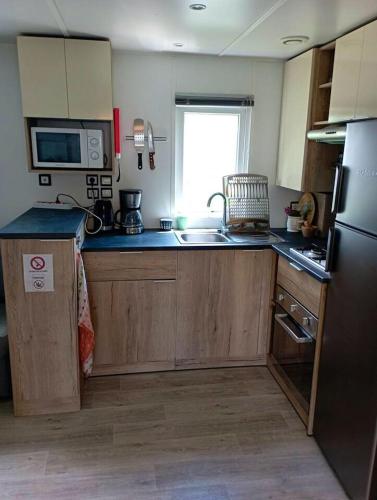 une cuisine avec des armoires en bois, un évier et un réfrigérateur dans l'établissement Bungalow confortable à Condrieu avec piscine partagée, à Condrieu