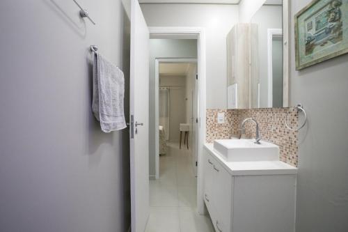 uma casa de banho branca com um lavatório e um espelho em Apartamento Praia do Tombo Guarujá 120m do mar no Guarujá