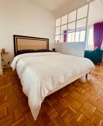 Cette chambre comprend un grand lit blanc et du parquet. dans l'établissement Vue imprenable sur la Tour Eiffeil, à Paris