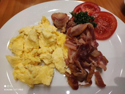 a white plate with scrambled eggs and bacon and a tomato at Hotel Königshof in Mainz