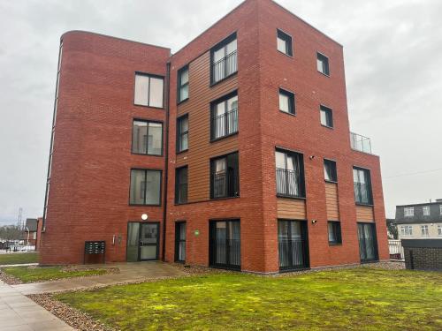 a red brick building with windows on a grass field at 1 Bed Apartment close to Heathrow Airport in Colnbrook