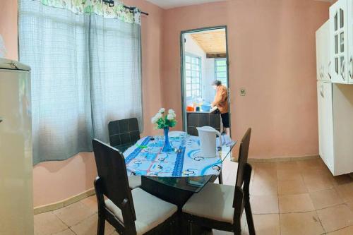 uma sala de jantar com uma mesa com cadeiras e uma pessoa na janela em Chácara Vale dos Eucaliptos em Pouso Alegre