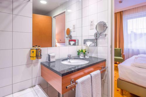 ein Bad mit einem Waschbecken und einem Bett in der Unterkunft Quality Hotel Vienna in Wien