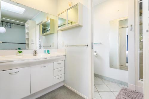 La salle de bains blanche est pourvue d'un lavabo et d'une douche. dans l'établissement Harbour Retreat with sea views and BBQ, à Whangaparaoa