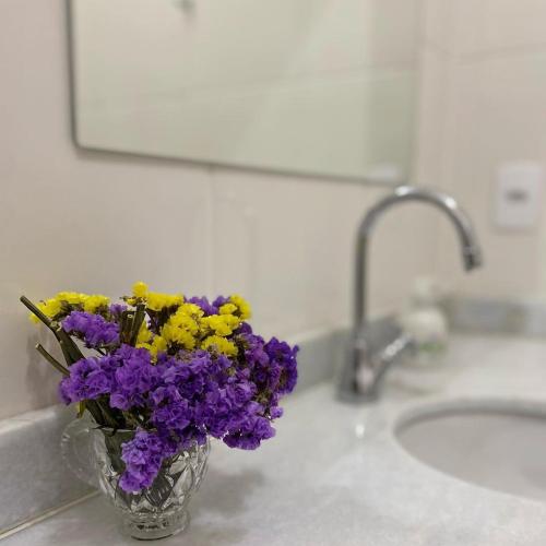 a vase of purple and yellow flowers on a bathroom counter at Quinta Vogrande no bairro de Águas Santas entre Tiradentes e São João Del Rey in Tiradentes