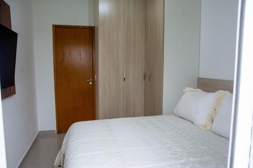 1 dormitorio con cama blanca y puerta de madera en Apartamento Primavera, en Boituva