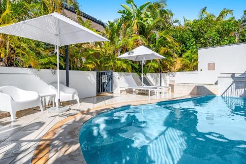 a swimming pool with chairs and umbrellas on a patio at Eco Beach Resort in Byron Bay