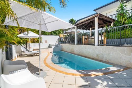 a swimming pool with a white umbrella and a house at Eco Beach Resort in Byron Bay