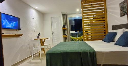 a bedroom with a bed and a table and a tv at MSFlats Paripueira Praia Wifi Ar Cozinha e Varanda Nascente c Rede in Paripueira