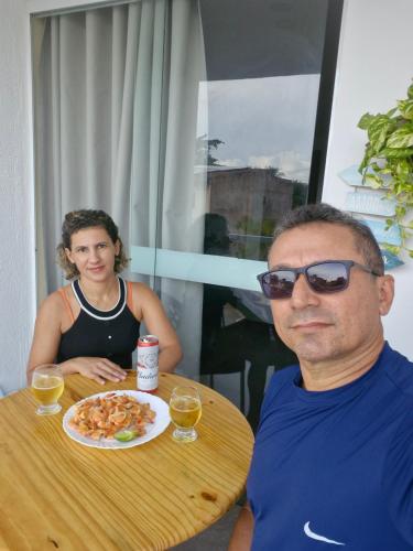 un homme et une femme assis à une table avec une assiette de nourriture dans l'établissement MSFlats Paripueira Praia Wifi Ar Cozinha e Varanda Nascente c Rede, à Paripueira