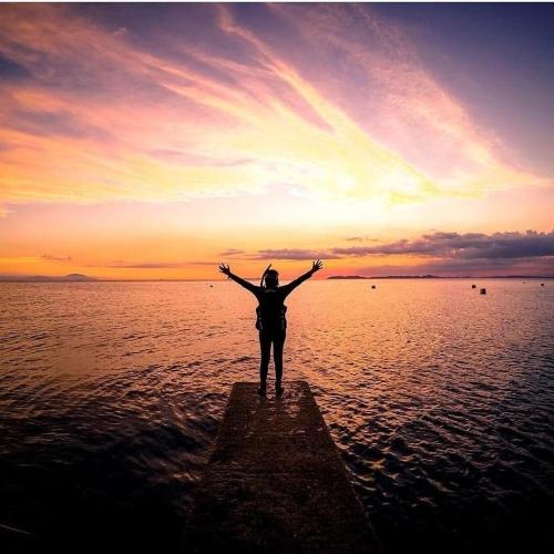 a person standing on a dock in the water at sunset at Dive and Trek Resort and Marine Sanctuary in Bauan