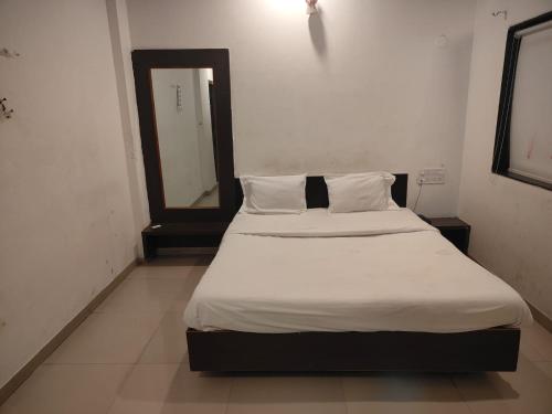 1 cama con sábanas blancas y espejo en una habitación en Sai Amaravathi Residency, en Shirdi